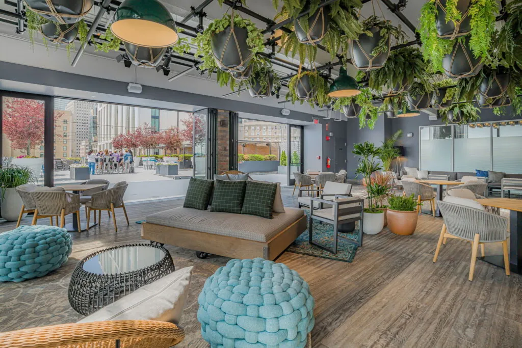 Modern indoor lounge with hanging plants, comfy chairs, and large windows—an inviting event space in downtown Boston with views of trees and city life.