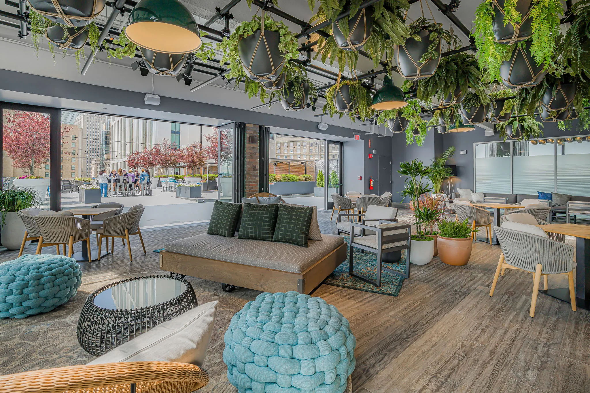 Modern indoor lounge with hanging plants, comfy chairs, and large windows—an inviting event space in downtown Boston with views of trees and city life.
