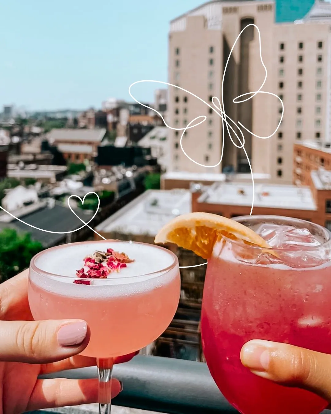 Two hands hold pink cocktails on a rooftop with a city view; a white butterfly and heart doodle overlay the image.
